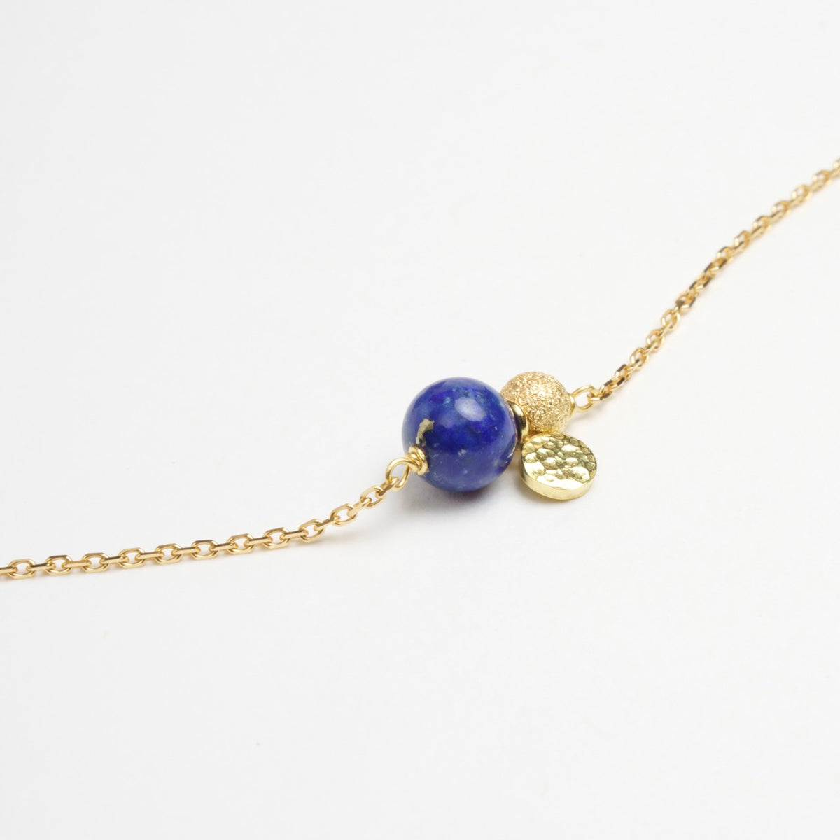 Delicate gold chain bracelet featuring rich Lapis Lazuli stone and textured gold sequin embellishment.