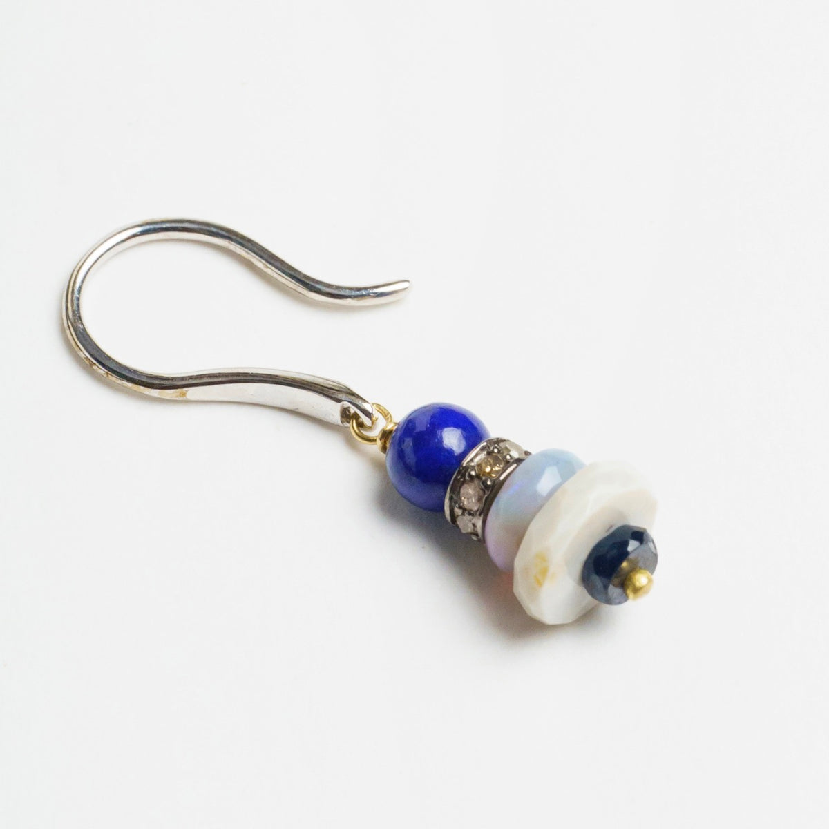 Colorful earrings featuring a stack of blue lapis lazuli, gray opal, and blue sapphire beads, with a white gold hook.