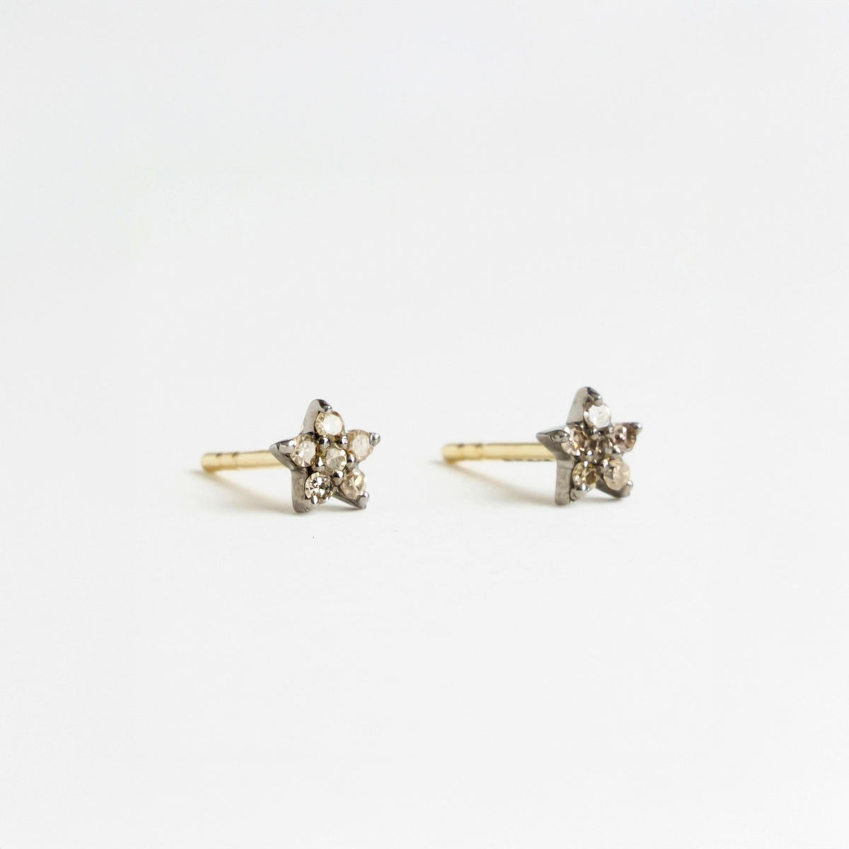 Silver and gold star-shaped earrings featuring salt and pepper diamonds, each 5mm in size.