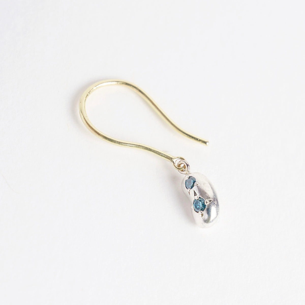 Mini Bean Drops earrings feature a silver bean design with two teal diamonds, suspended from 18ct yellow gold hooks.