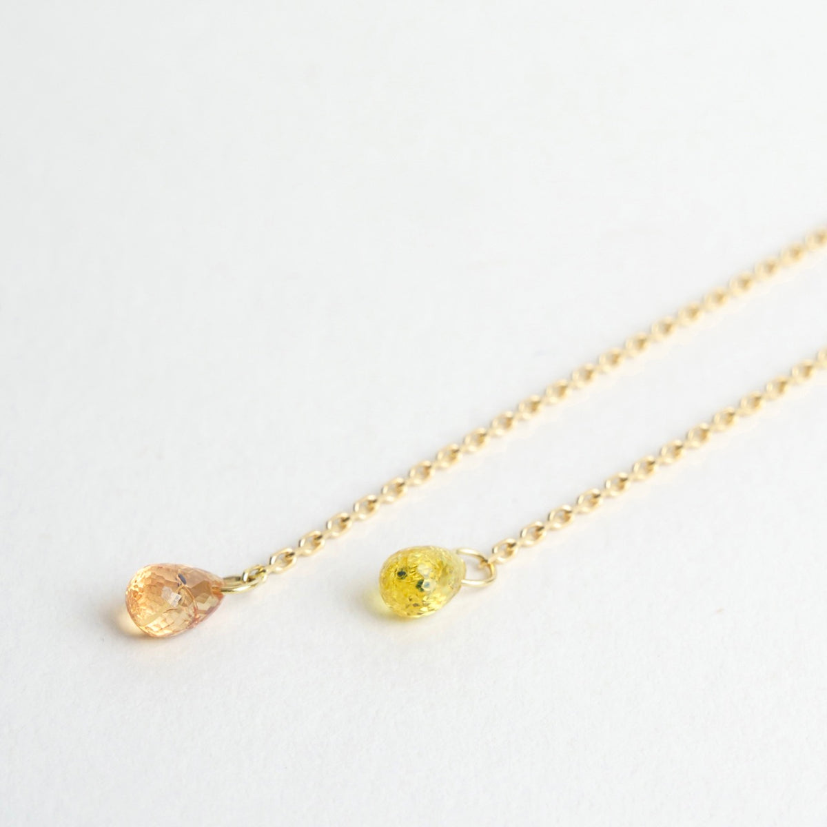 Sapphire briolettes in shades of pink and yellow drop from refined 18ct yellow gold chains, measuring 10cm in length.