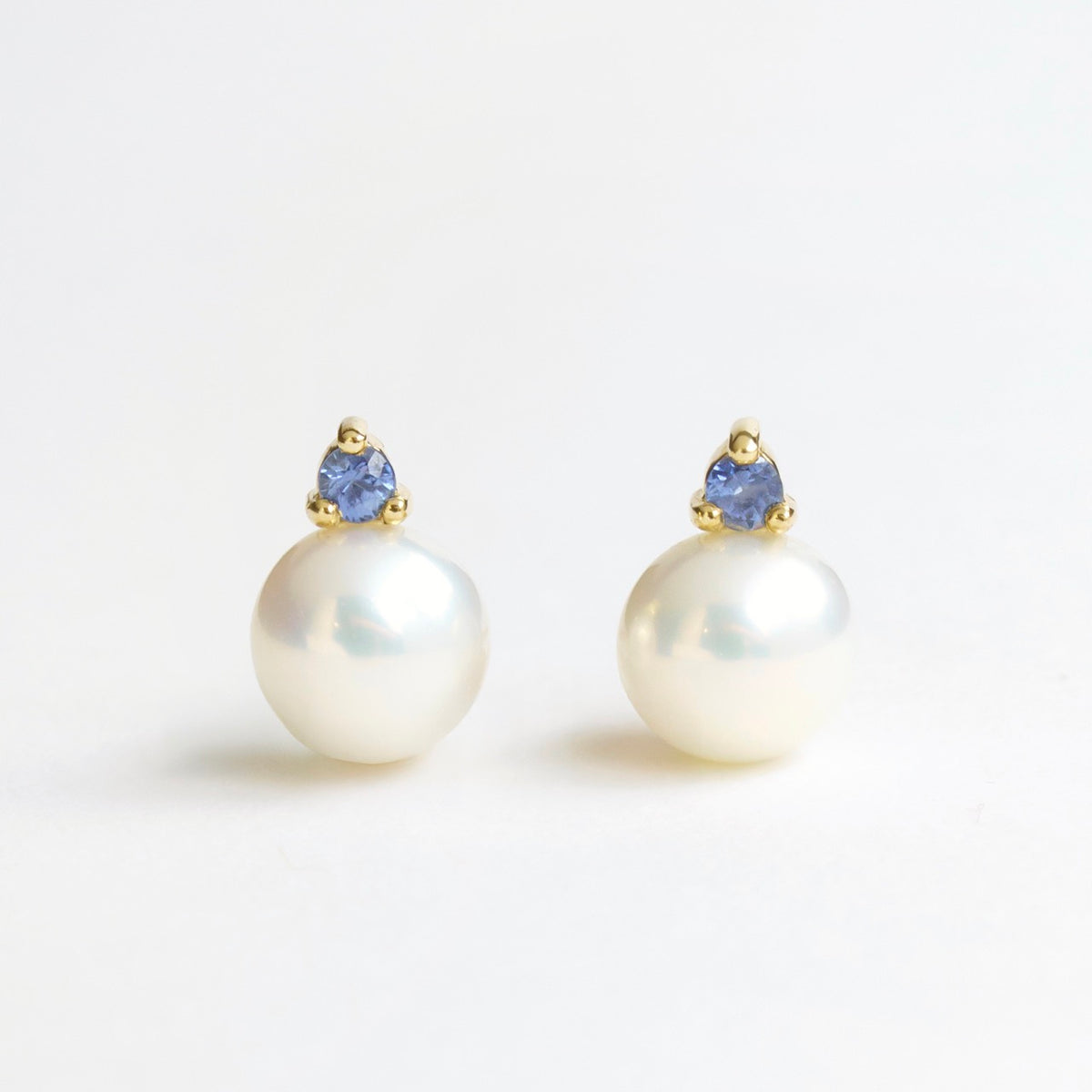 Lustrous freshwater pearl earrings featuring a blue sapphire and 18ct yellow gold setting.