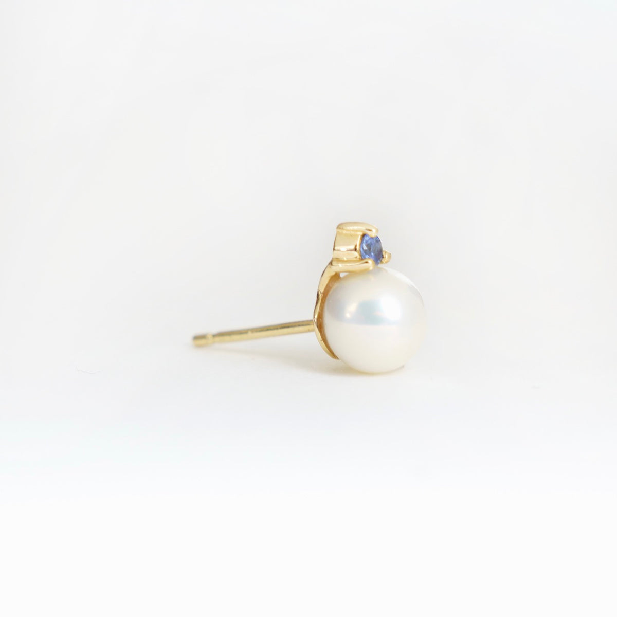 Lustrous 6mm freshwater pearl earrings in 18ct yellow gold, accented with a small blue sapphire.