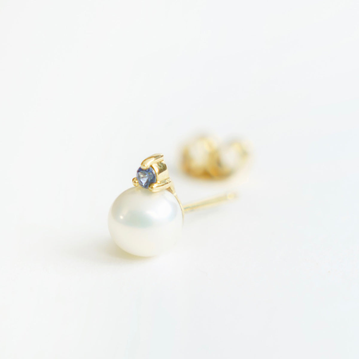 Lustrous 6mm freshwater pearl earrings in 18ct yellow gold, featuring a blue sapphire accent on top.