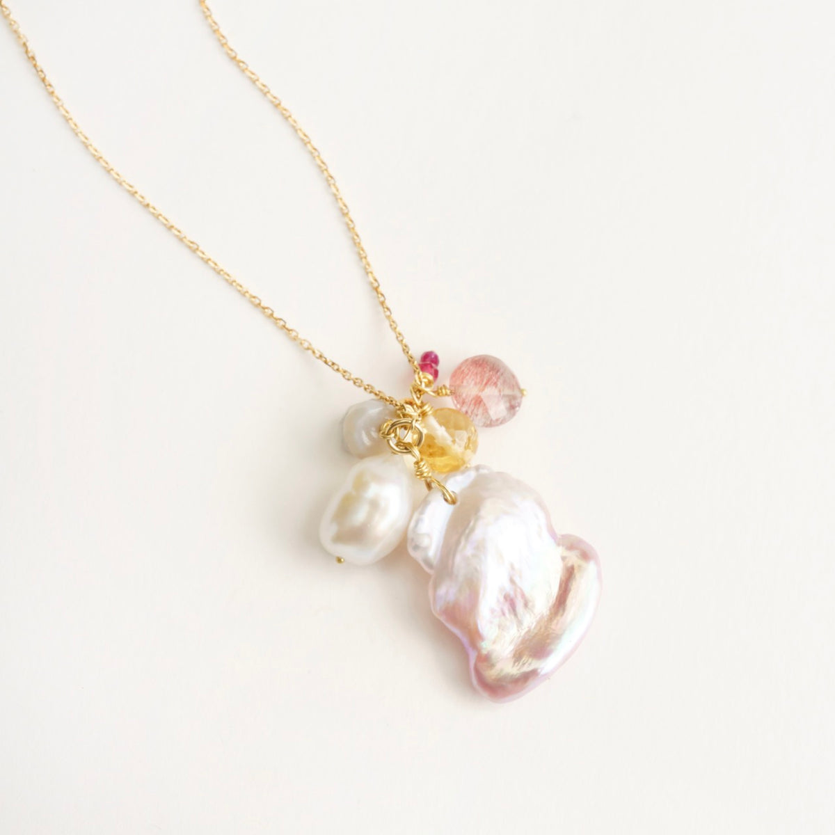 Cluster necklace featuring a large organic pink pearl, white baroque pearls, and colorful gemstones on an 18ct yellow gold chain.