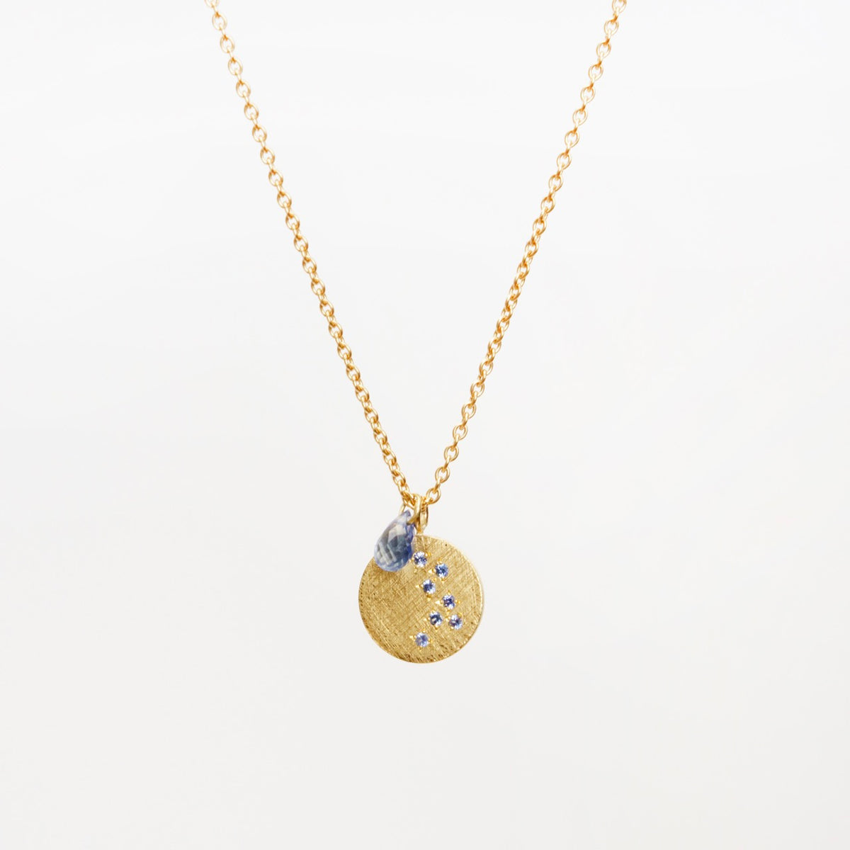 18ct yellow gold necklace featuring a textured round pendant with sapphires, hung on a flat curb chain.