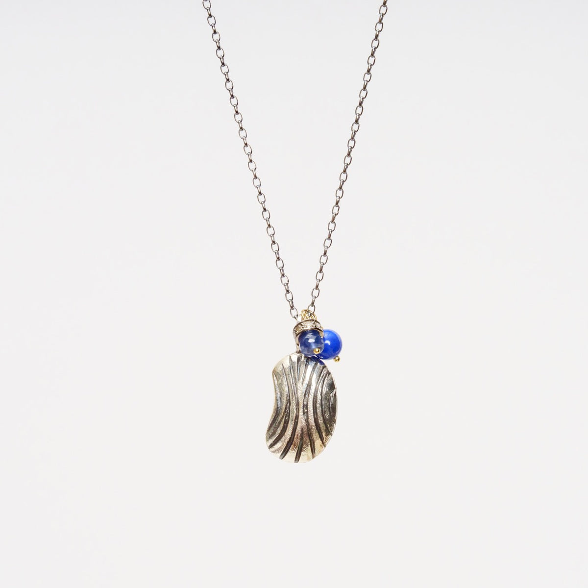 Carved Bean Pendant 2 on a 22" blackened sterling silver chain with a textured silver bean and blue lapis lazuli bead.