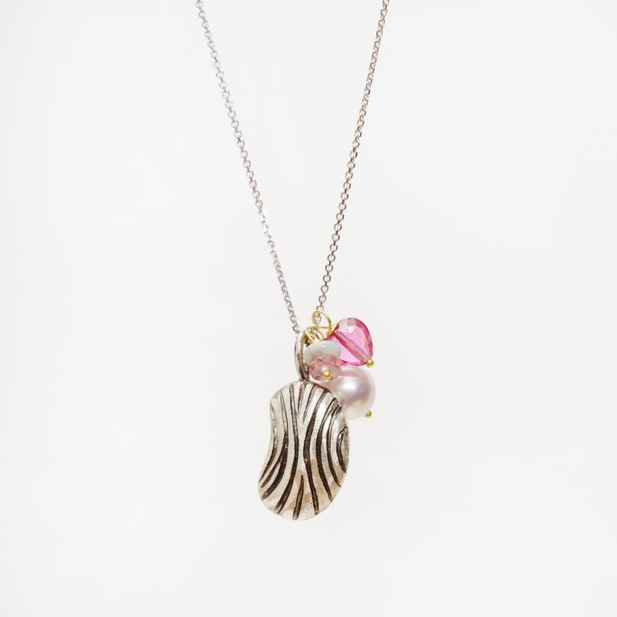 Carved silver bean pendant with a freshwater pearl, pink tourmaline heart, and small gemstones on a delicate chain.