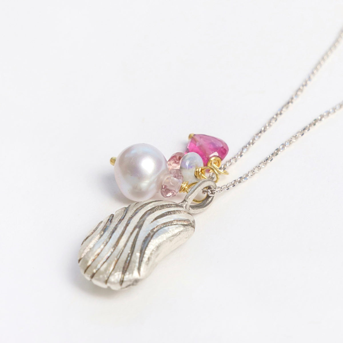 Sterling silver pendant with a textured carved bean design, featuring a freshwater pearl and pink gemstones.