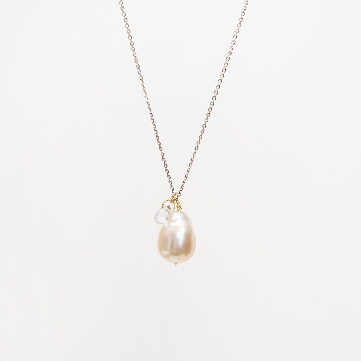 Icy white gold chain necklace featuring a baroque pearl pendant with a small blue sapphire drop attached.