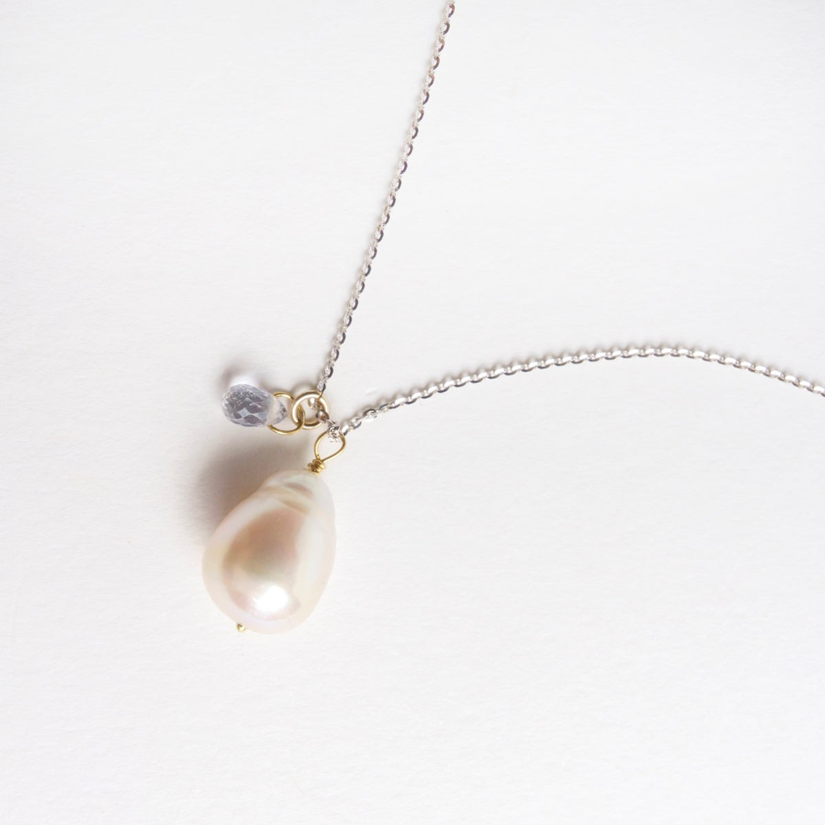 Icy white gold chain featuring a baroque pearl and an icy blue sapphire drop, showcasing elegant design details.