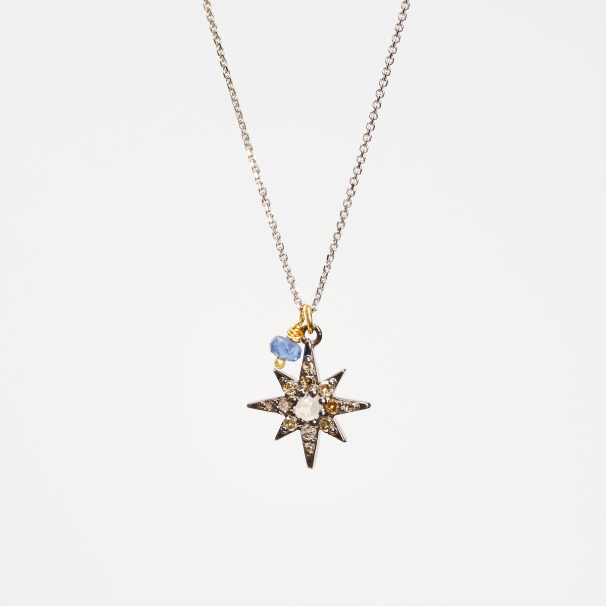 Southern Star Necklace featuring a blackened sterling silver star set with diamonds and a blue sapphire detail, on a white gold chain.