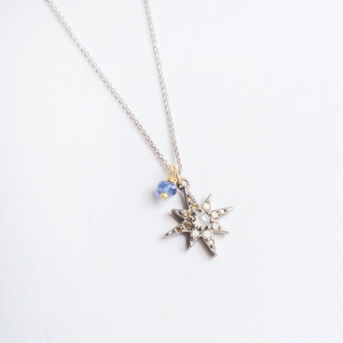 Blackened sterling silver star pendant with diamonds and blue sapphire detail on a silver chain, 20" long.