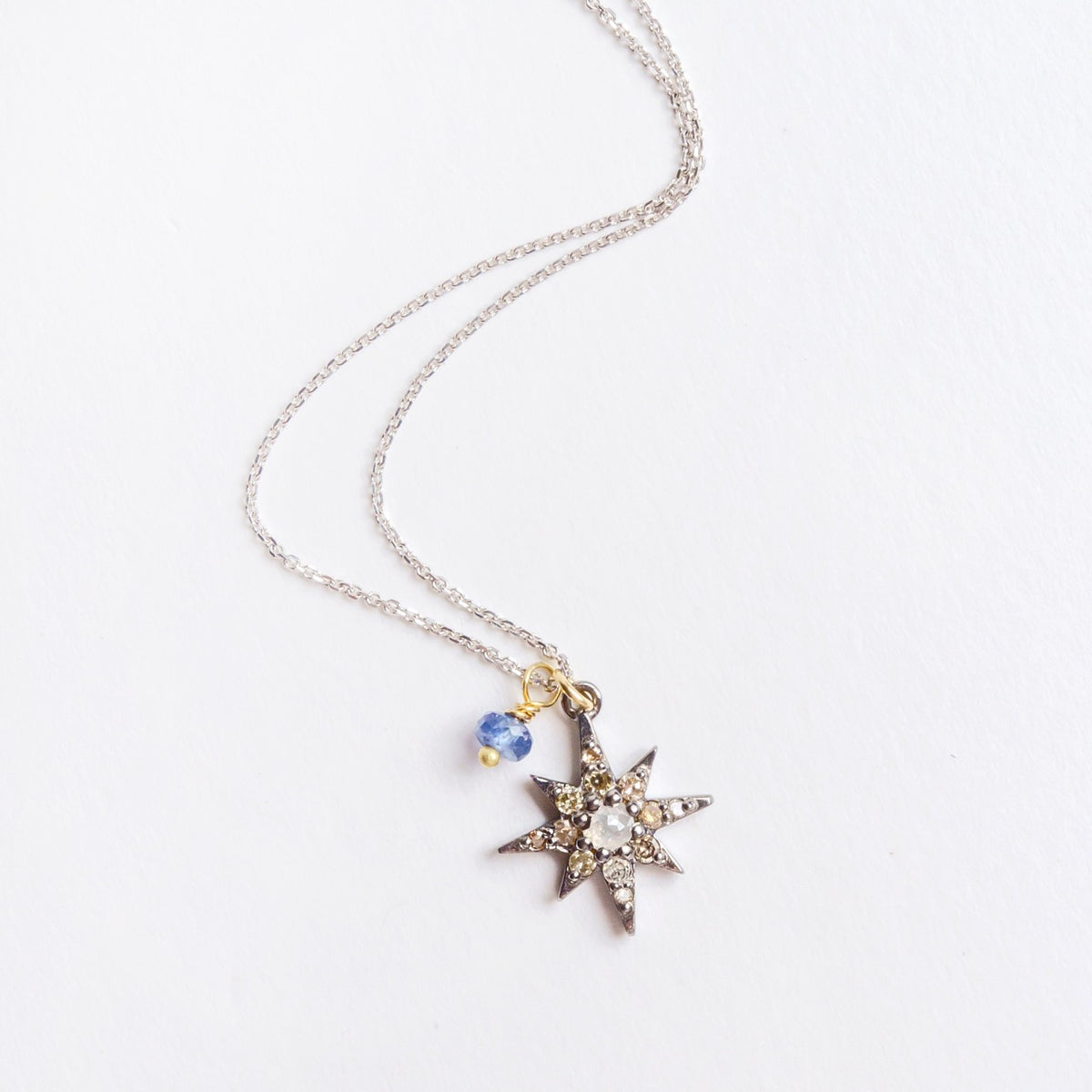 Blackened sterling silver star necklace featuring a rose cut diamond center and a blue sapphire detail on a silver chain.