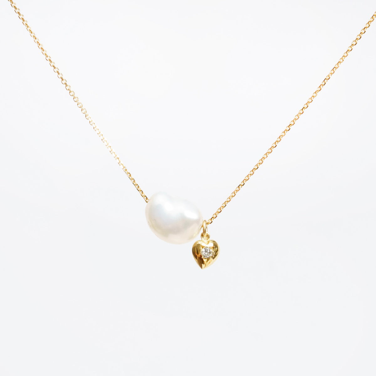 Lustrous cloud-shaped freshwater pearl on an 18ct yellow gold chain, featuring a tiny gold heart with a silver diamond.