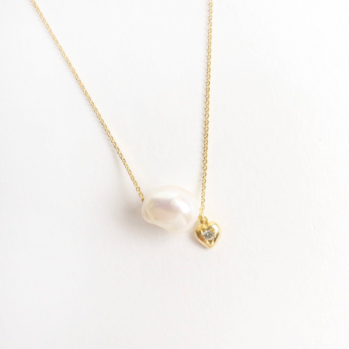 Lustrous cloud-shaped freshwater pearl on an 18ct yellow gold chain, paired with a small gold heart and silver diamond.