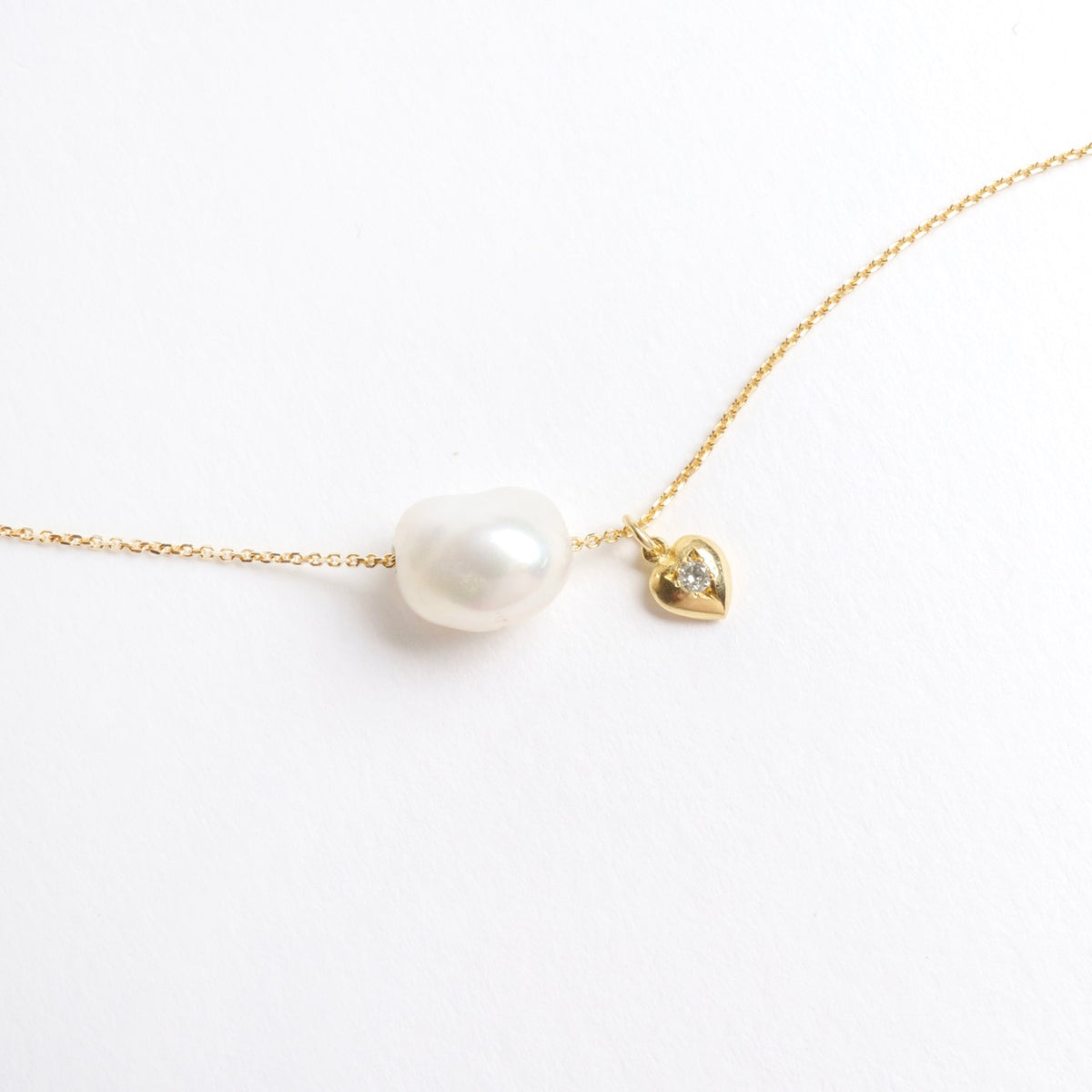 Lustrous cloud-shaped freshwater pearl on an 18ct yellow gold chain, featuring a small gold heart with a diamond.