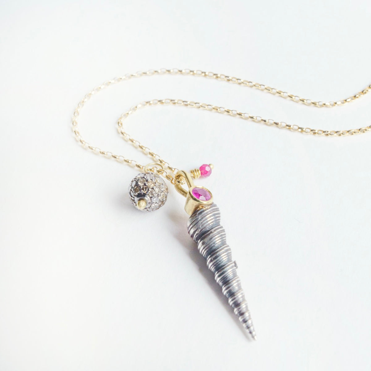 Silver shell pendant on an 18ct yellow gold chain, featuring rubies and champagne diamonds with a unique texture.