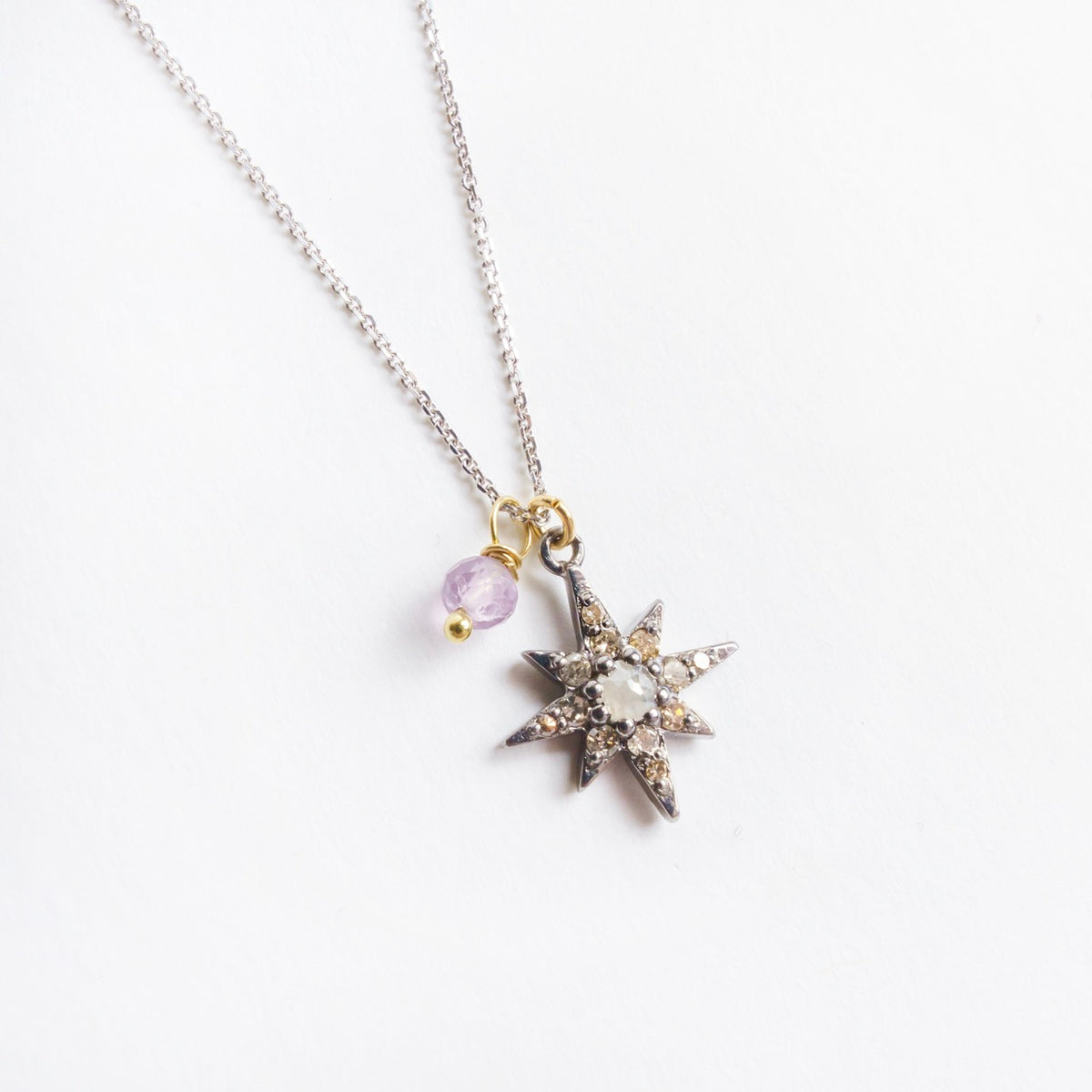 Southern Star Necklace features a silver star pendant adorned with diamonds and a lavender spinel detail on a gold pin.