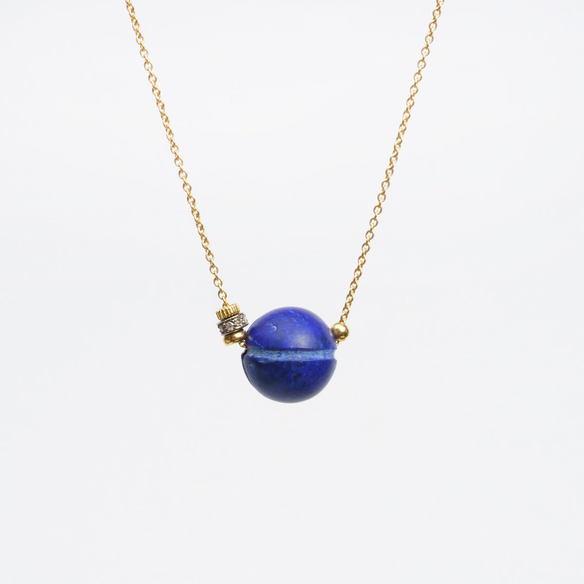 Hippy Trail Necklace 2 features an 18ct yellow gold chain and a round lapis lazuli pendant with diamond detailing.