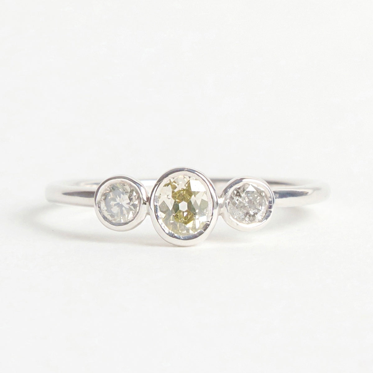 Trilogy ring with three mixed-tone diamonds set in an 18ct white gold band, featuring round and oval shapes.