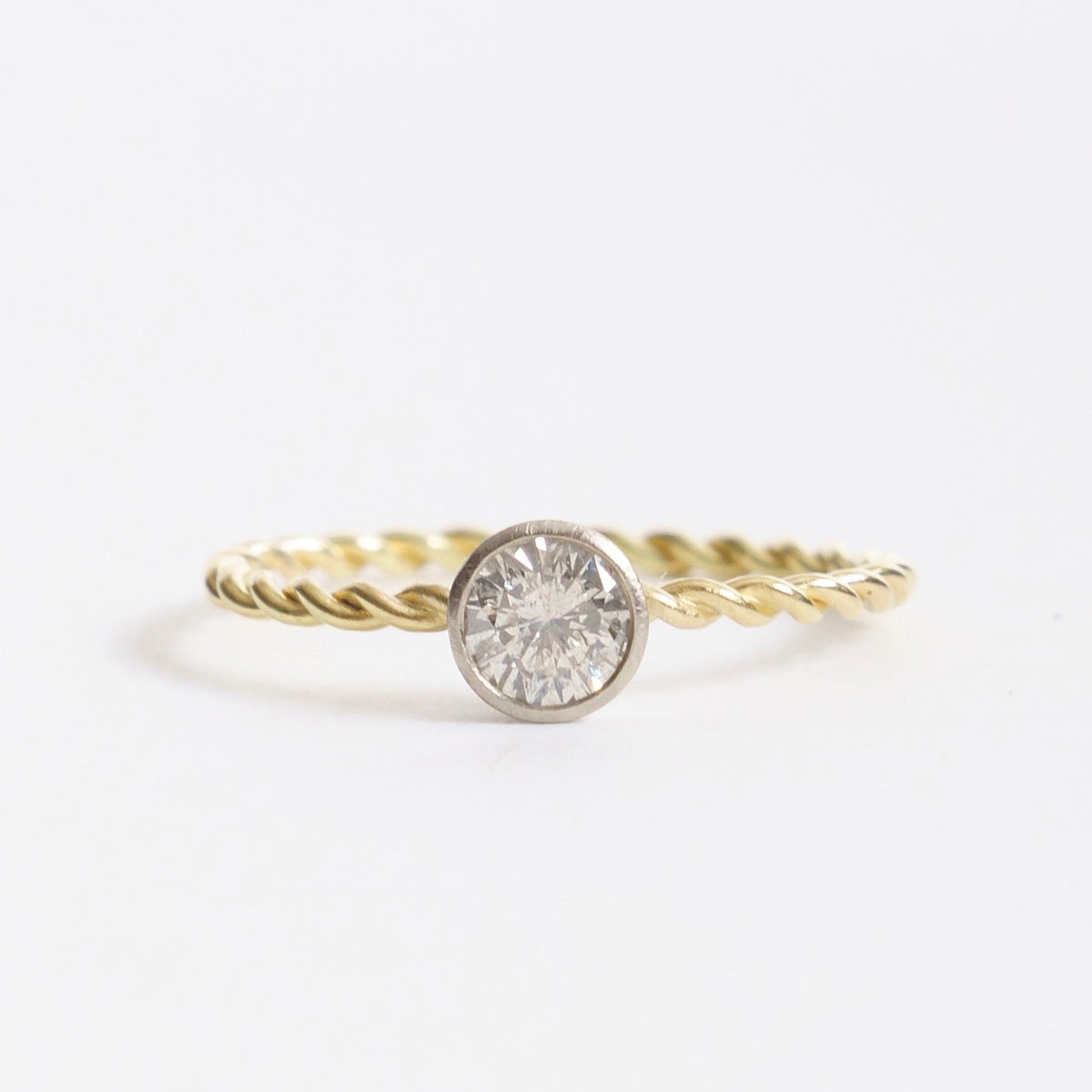 Twisted 18ct yellow gold ring featuring a round silver diamond centerpiece set in a white gold bezel.