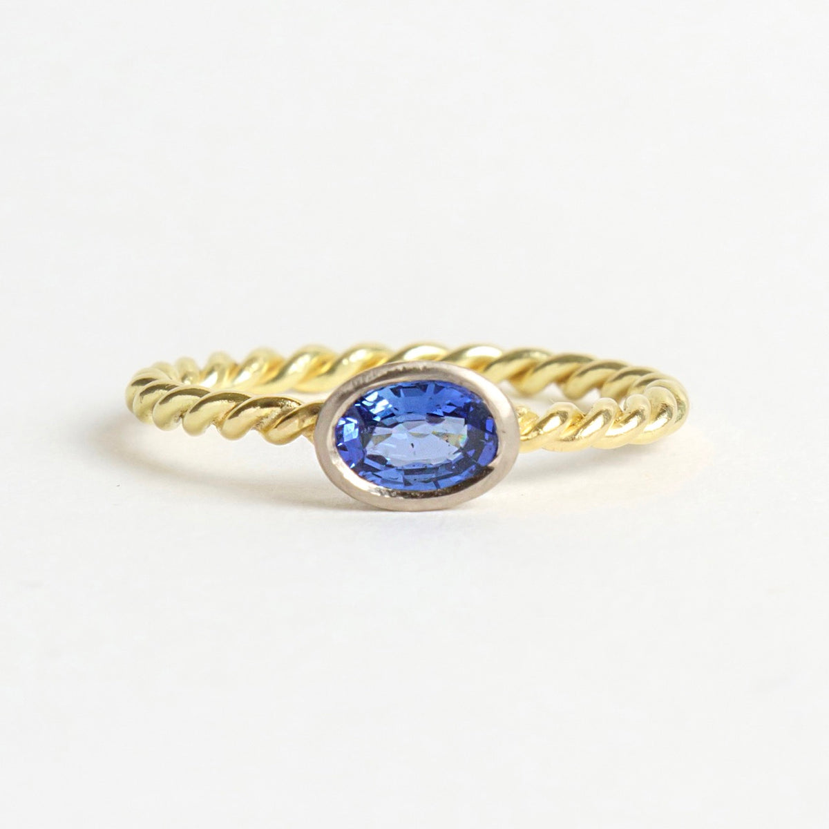 Blue sapphire set in a white gold bezel, on a twisted 18ct yellow gold band, showcasing a rich blue hue.