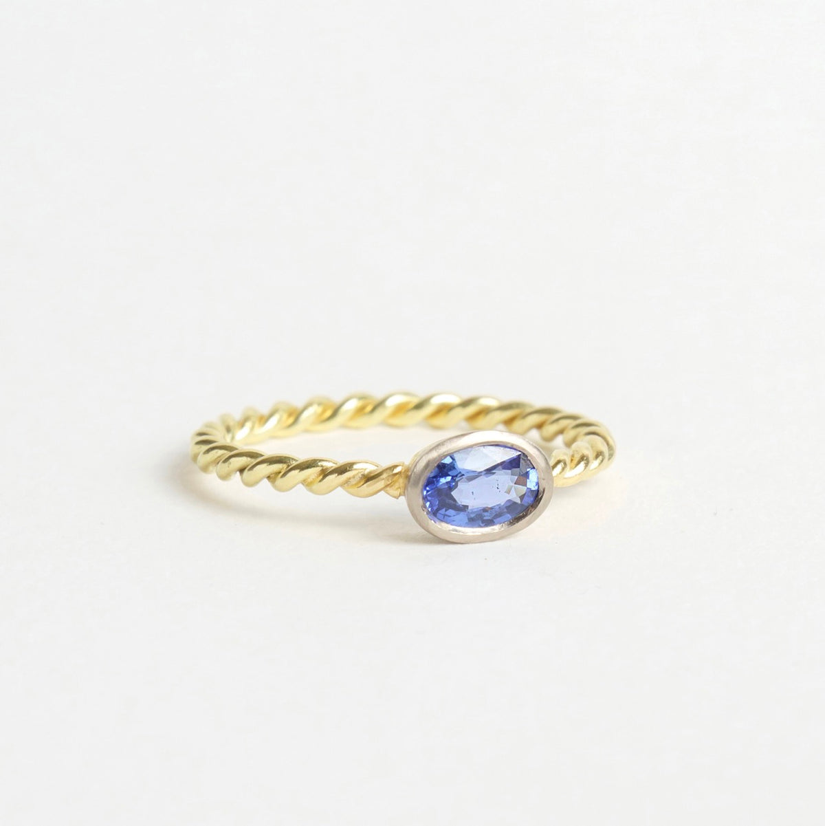 Rich blue sapphire set in a white gold bezel on a twisted 18ct yellow gold band. Elegant and handmade.