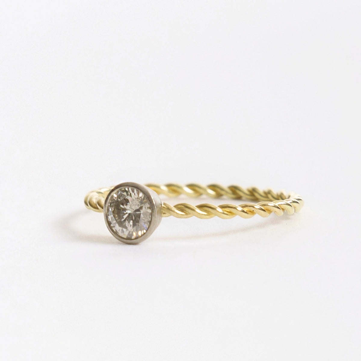 Silver diamond ring with a twisted 18ct yellow gold band and a round, bezel-set stone.