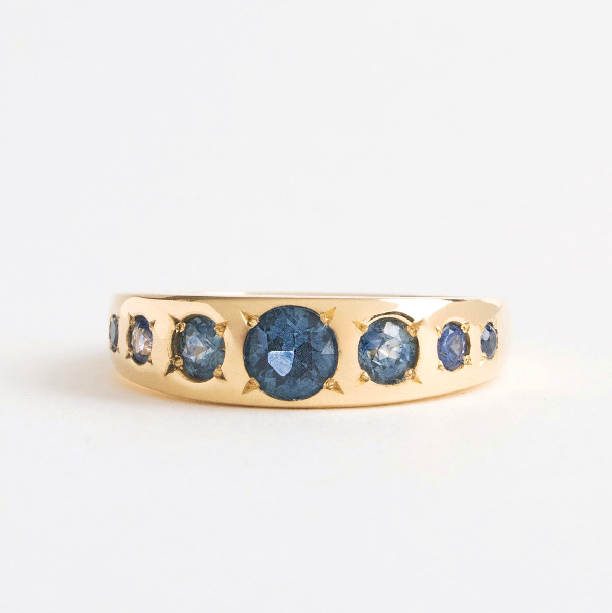 Seven Sisters Band Ring featuring seven blue sapphires set in 18ct yellow gold, tapering design from 6mm to 3mm.