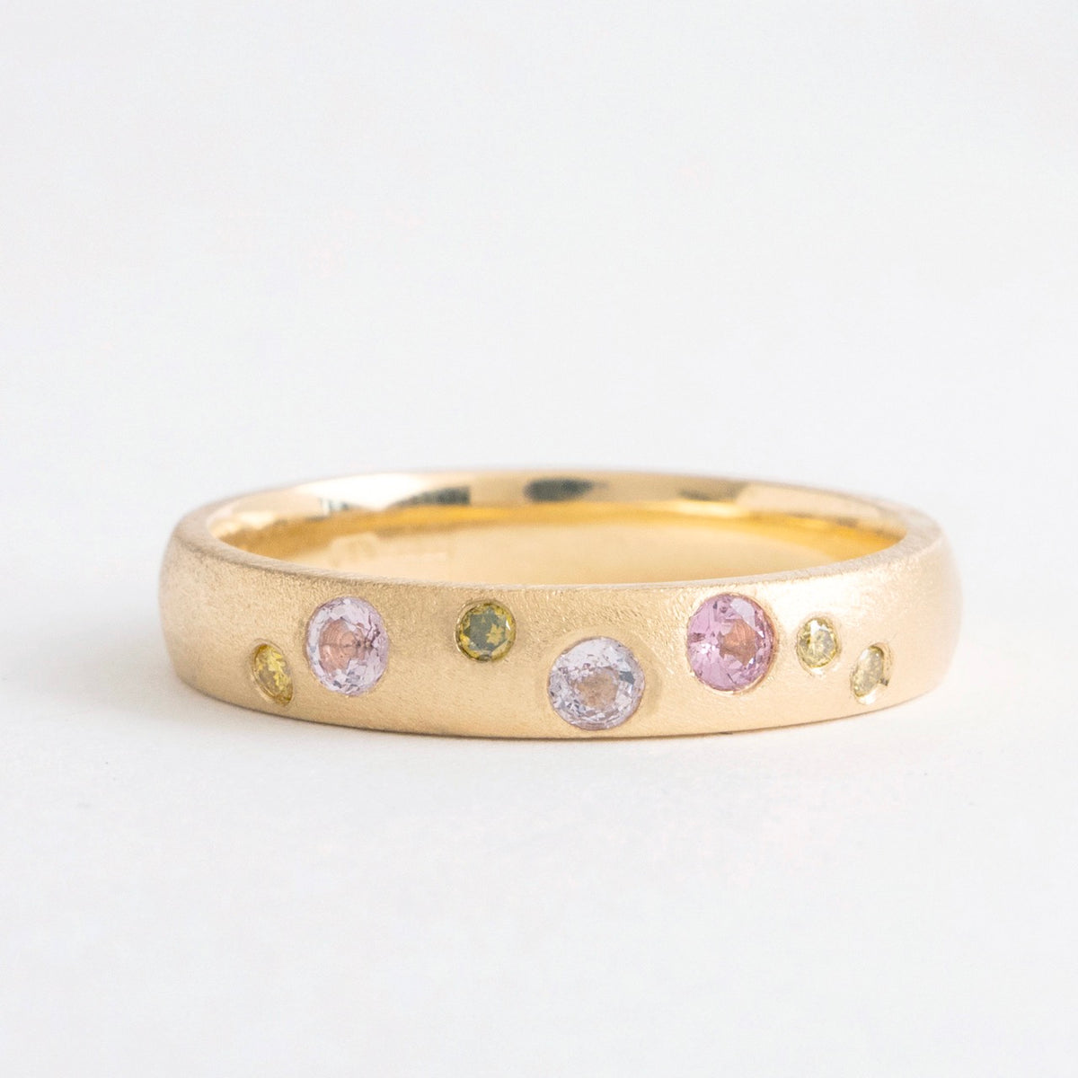 Wide band ring in 18ct yellow gold featuring scattered pink spinels and yellow diamonds. Elegant matte finish.