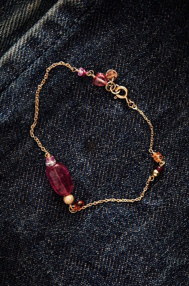 Bracelet with red beads and gold chain on a dark denim background